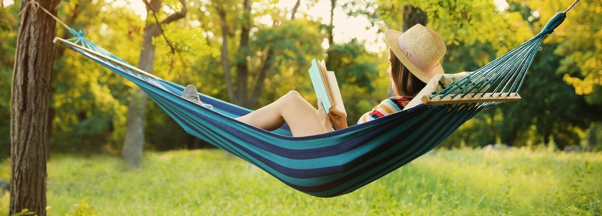 Vrouw leest een boek in een hangmat in de tuin