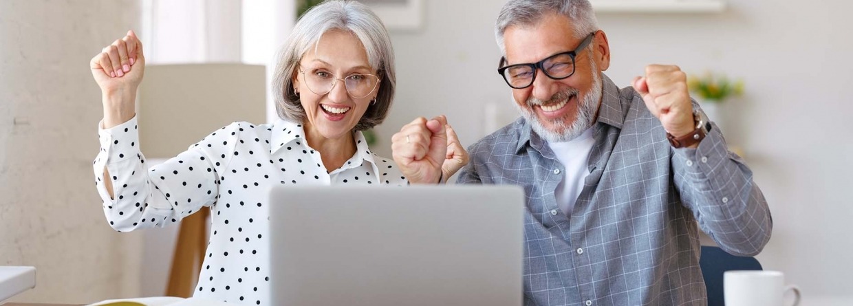 Blij senioren stel dat thuis aan de tafel achter de laptop zit