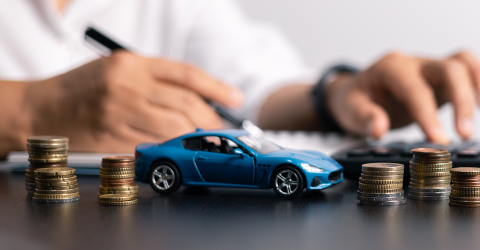 Man achter bureau met een pen, rekenmachine, miniatuur auto en stapels muntgeld